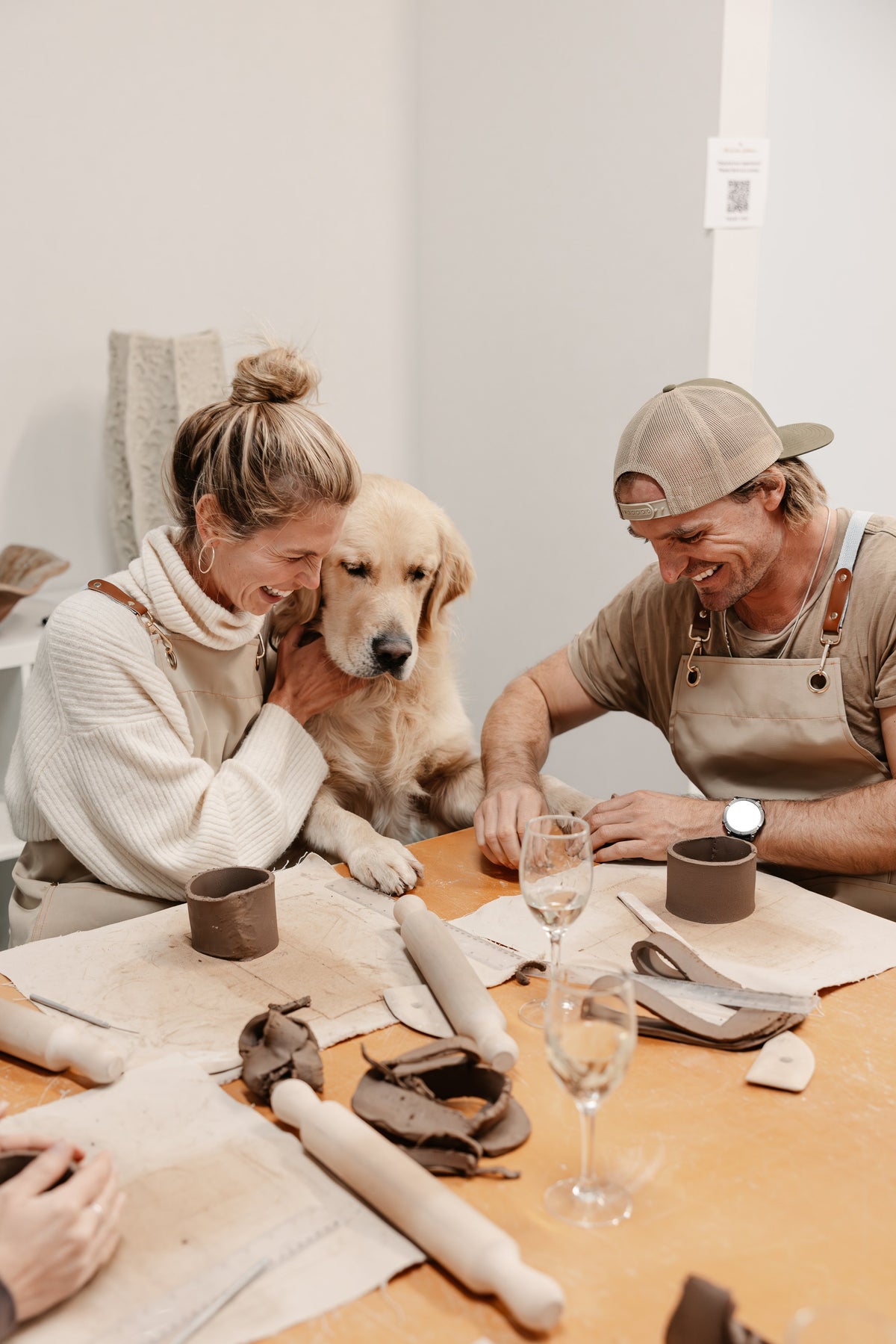 Two guests hand building ceramics at the studio workshop table, a dog beside them